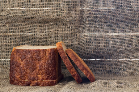 A sliced loaf of black bread on a dark burlap background