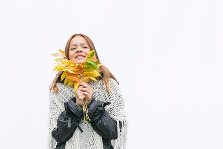 A young girl in a warm jacket with autumn leaves on a white background