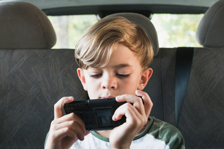 A little boy is sitting in a car and playing a game on his phone