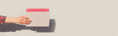 A person's hand holds a red gift box made of thick paper on a light backgroundの写真素材