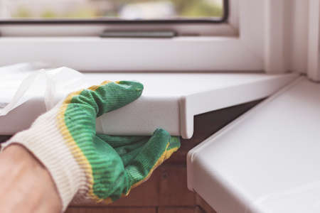 A worker in gloves sets the window sills on the balcony frame. The material is white plasticの写真素材