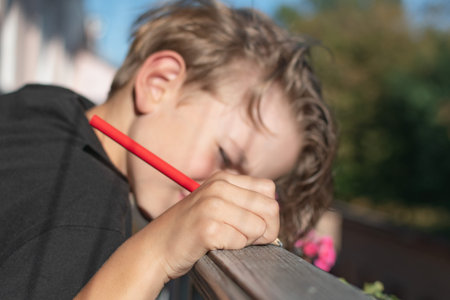 A little boy is bored sitting on the balcony. Draws with a pencil on the railing.