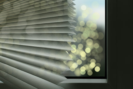 Fragment of paper blinds for a white plastic window. Holiday lights on the street