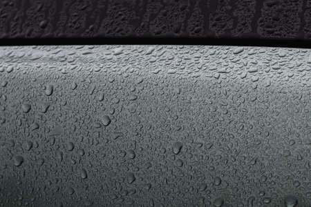 A fragment of a dark colored car body covered with raindropsの写真素材