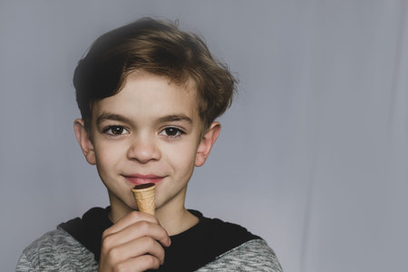 A little boy with brown eyes holds a sweet cake in his hand