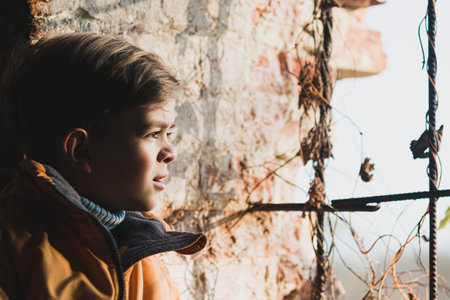 A little boy looks through an old window with bars in an ancient fortress at sunsetの写真素材
