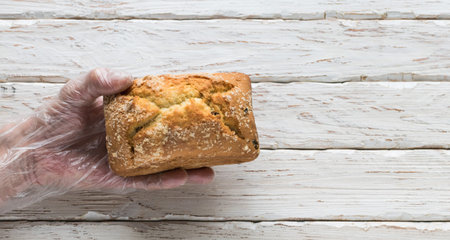 Men's hands in protective gloves hold a loaf of bread on a light decorative background
