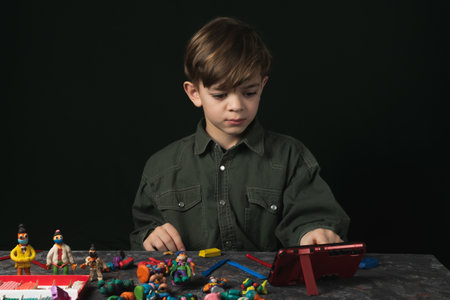a small boy sits at a table and sculpts from plasticine on a dark backgroundの写真素材