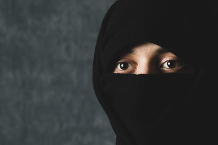 A young guy with brown eyes in a balaclava poses in front of the camera on a dark backgroundの写真素材
