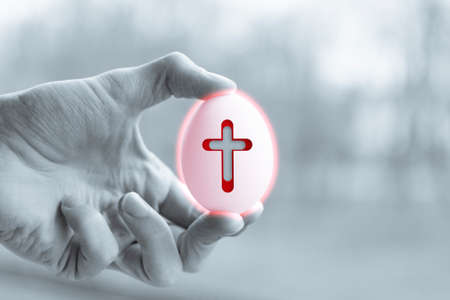 Human hands hold a chicken egg with cross symbolの写真素材