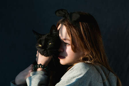 Young girl plays with a black pet cat during sunsetの写真素材