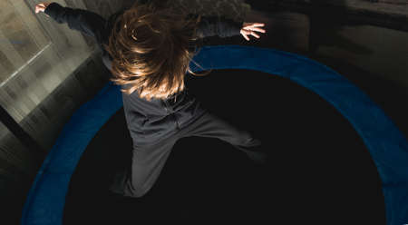 A little boy jumps on a round trampoline with a safety net in an apartmentの写真素材