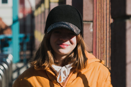 Portrait image of a young girl in a yellow jacket and cap in the spring sunの写真素材