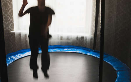 Blurry image, a little boy resting after jumping on a circular trampoline with a safety net in an apartmentの写真素材