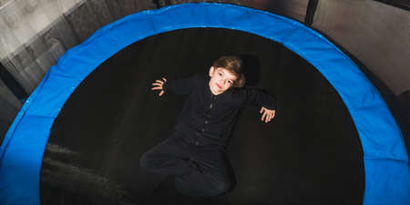 A little boy rests after jumping on a round trampoline with a safety net in an apartmentの写真素材