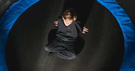 A little boy rests after jumping on a round trampoline with a safety net in an apartment