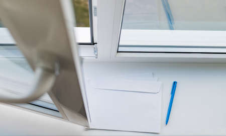 A letter envelope and a pen on the sill of an open windowの写真素材