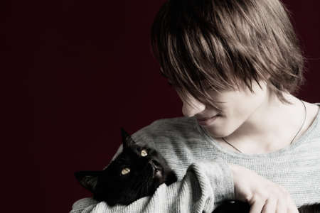 A young guy with long hair holds a black cat in his hands.の写真素材