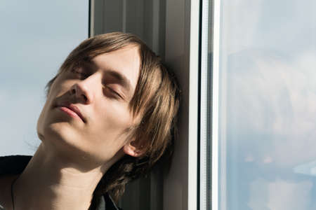 Portrait image of a young guy near the window on a sunny dayの写真素材