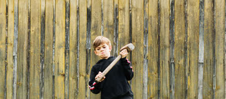 A small boy in a black jacket works with a large sledgehammerの写真素材