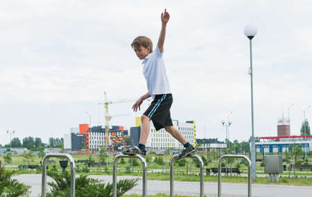 A little boy in a white T-shirt is playing in the park, jumping on a metal railingの写真素材