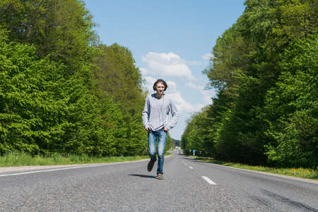 A young guy with headphones is walking along the road and listening to music through his phoneの写真素材