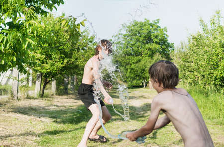 A little boy douses himself with water with his older brother in natureの写真素材