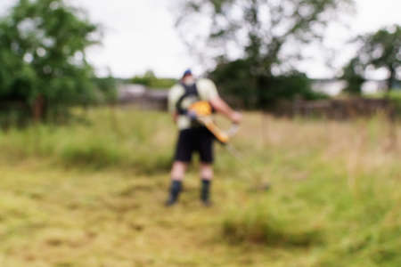 Blurred image of a man mowing grass on a plot in a country houseの写真素材