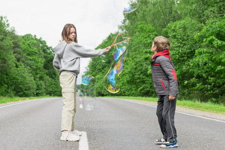 Brother and sister are playing on the highway outside the city, blowing soap bubblesの写真素材
