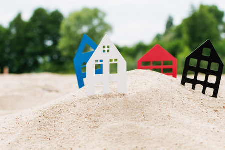 Metal models of houses of different colors stand in the sand