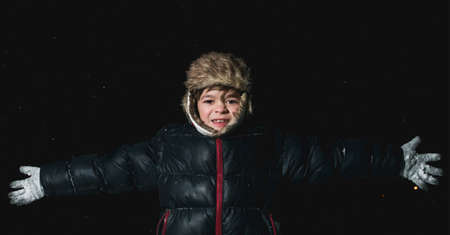 Photo of a boy in winter clothes in the evening in snowy frosty weather, playing in the darkの写真素材