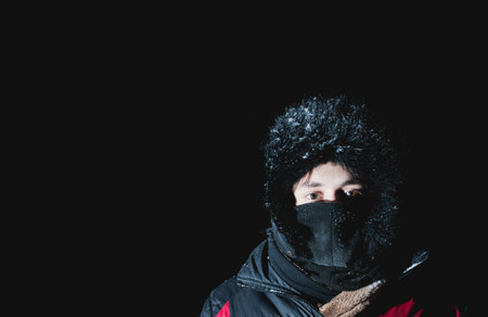 A young guy is wrapped up in winter clothes at night