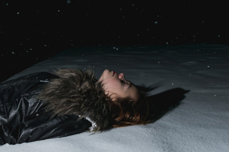 A young girl plays in the snow at night near a lantern