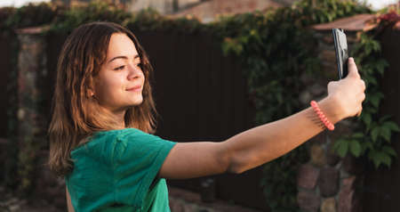 A young girl is photographed on her phone in the gardenの写真素材