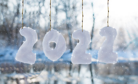 A river covered with ice and snow. Snow icicles in the form of the numbers 2022 hang on the branches