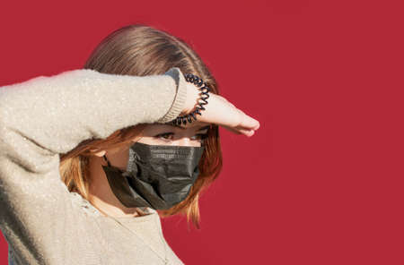 A young girl in a protective medical mask looks at the sunの写真素材