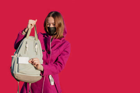 A young girl in a warm coat in a protective medical mask with a backpack, a badge and a QR codeの写真素材
