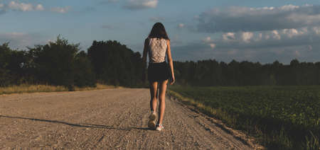 A young girl walks along a country road during sunsetの写真素材