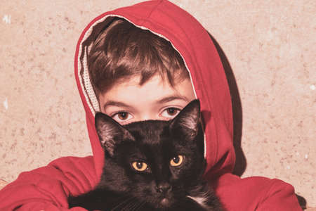 Portrait image of a little boy in a red T-shirt with a cat in his handsの写真素材