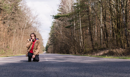 Tinted portrait image of a young guy in a hooded jacket on a forest road outside the cityの写真素材