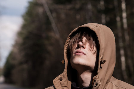 Tinted portrait image of a young guy in a hooded jacket on a forest road outside the cityの写真素材