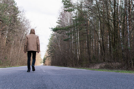 Tinted portrait image of a young guy in a hooded jacket on a forest road outside the cityの写真素材