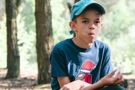 A little boy eats in the forest sitting on a chair during a picnicの写真素材