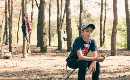 A little boy eats in the forest sitting on a chair during a picnicの写真素材