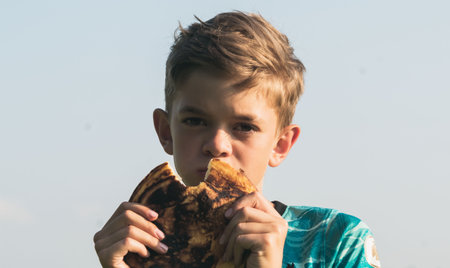Little boy eats a big pancake outdoorsの写真素材