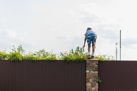A little boy climbs over a metal fence on a private plotの写真素材