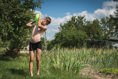A little boy is doused with water in the courtyard of a country house in hot weather