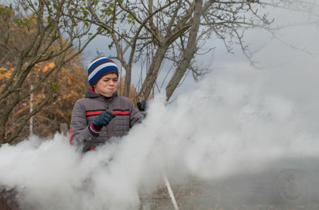 A teenage boy burns autumn leaves in a metal barrel on a country plotの写真素材