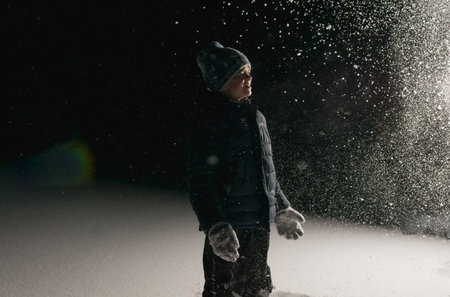 A little boy is playing in the thick snow at night with one light source
