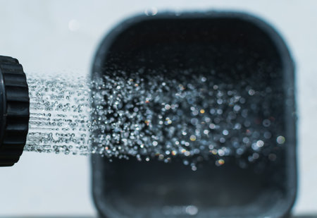 Splashes of water pouring from a watering tap into a plastic container in the backyardの写真素材